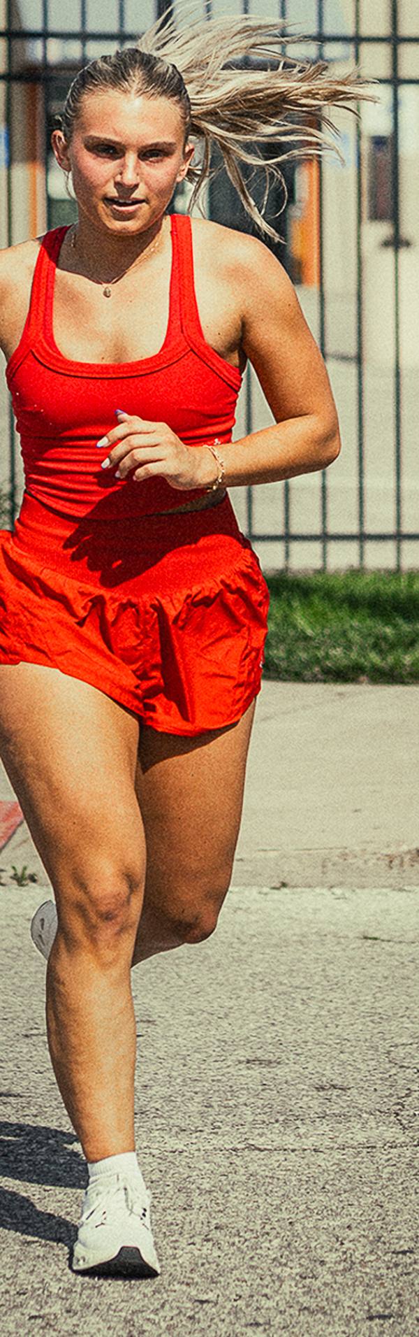 A runner in an orange top and shorts mid-stride on a St. Louis sidewalk.